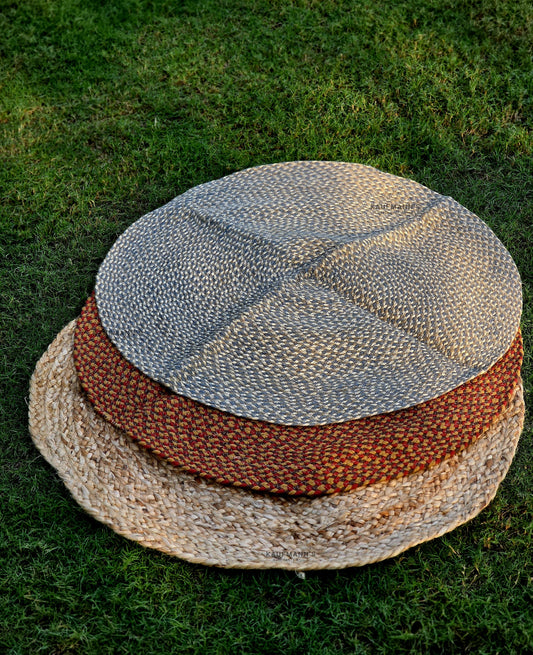 Two braided rugs in orange and brown colors are displayed on a round, beige straw mat, placed on a grassy surface.