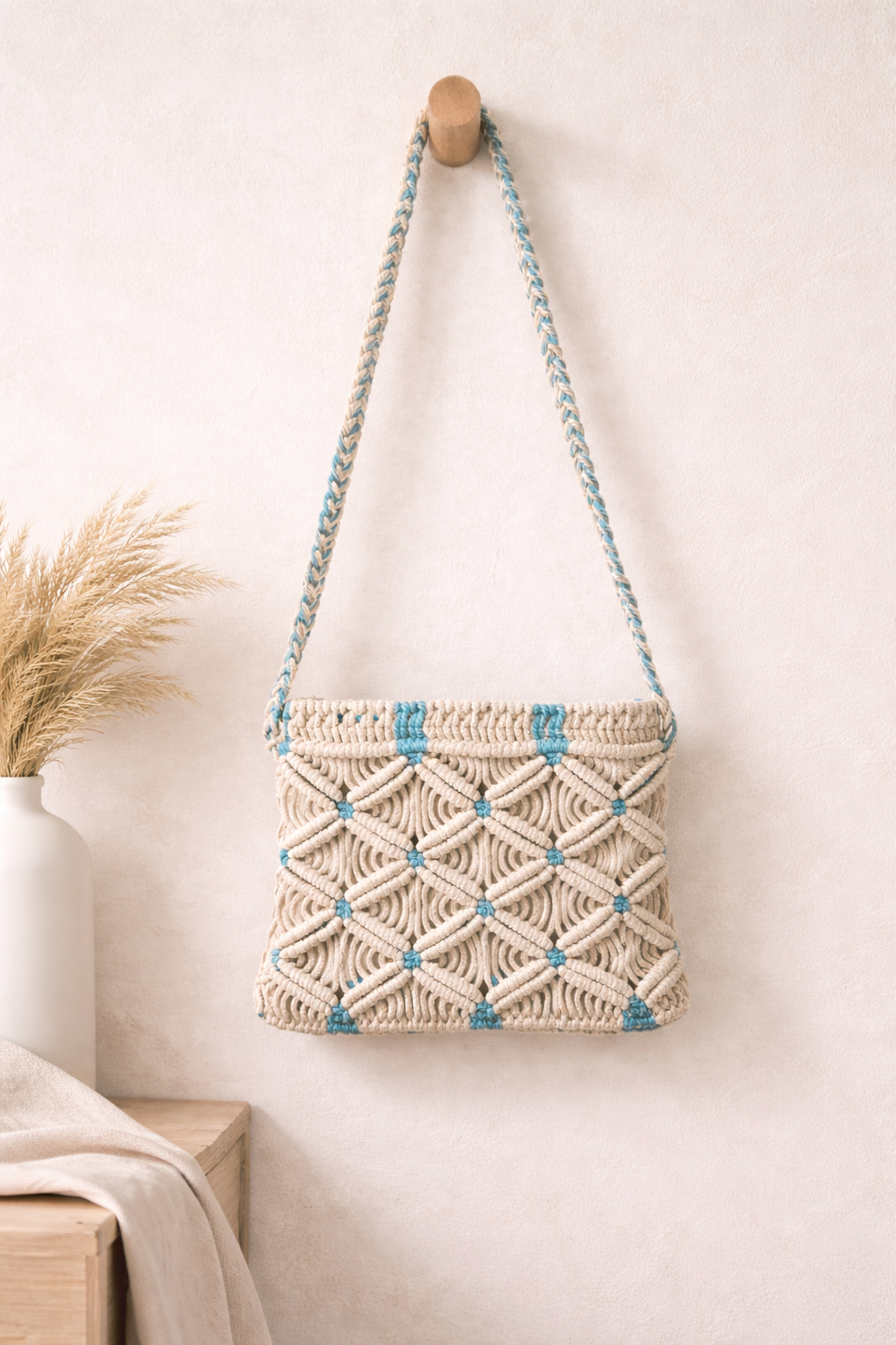 Macrame handbag with blue accents hanging on a wooden hook against a light background