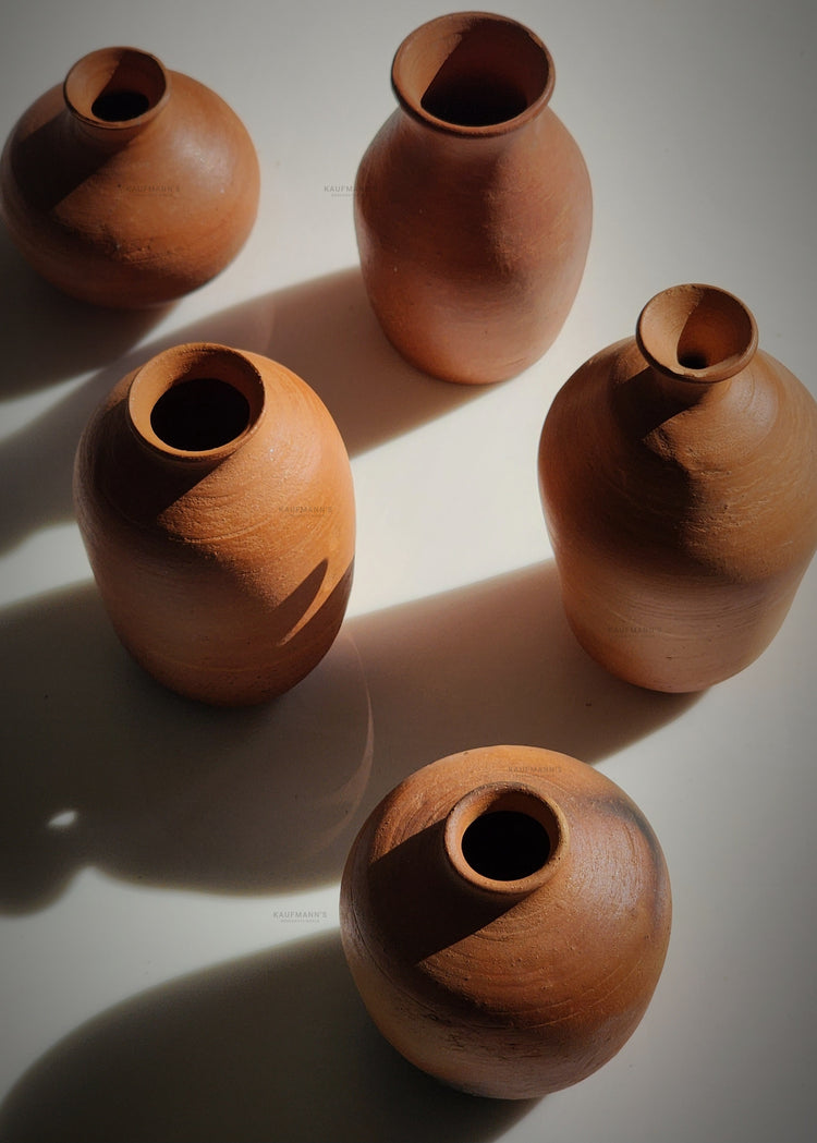 Five terracotta pots and miniature terracotta pots arranged on the floor under natural sunlight, casting soft shadows in a rustic setting.