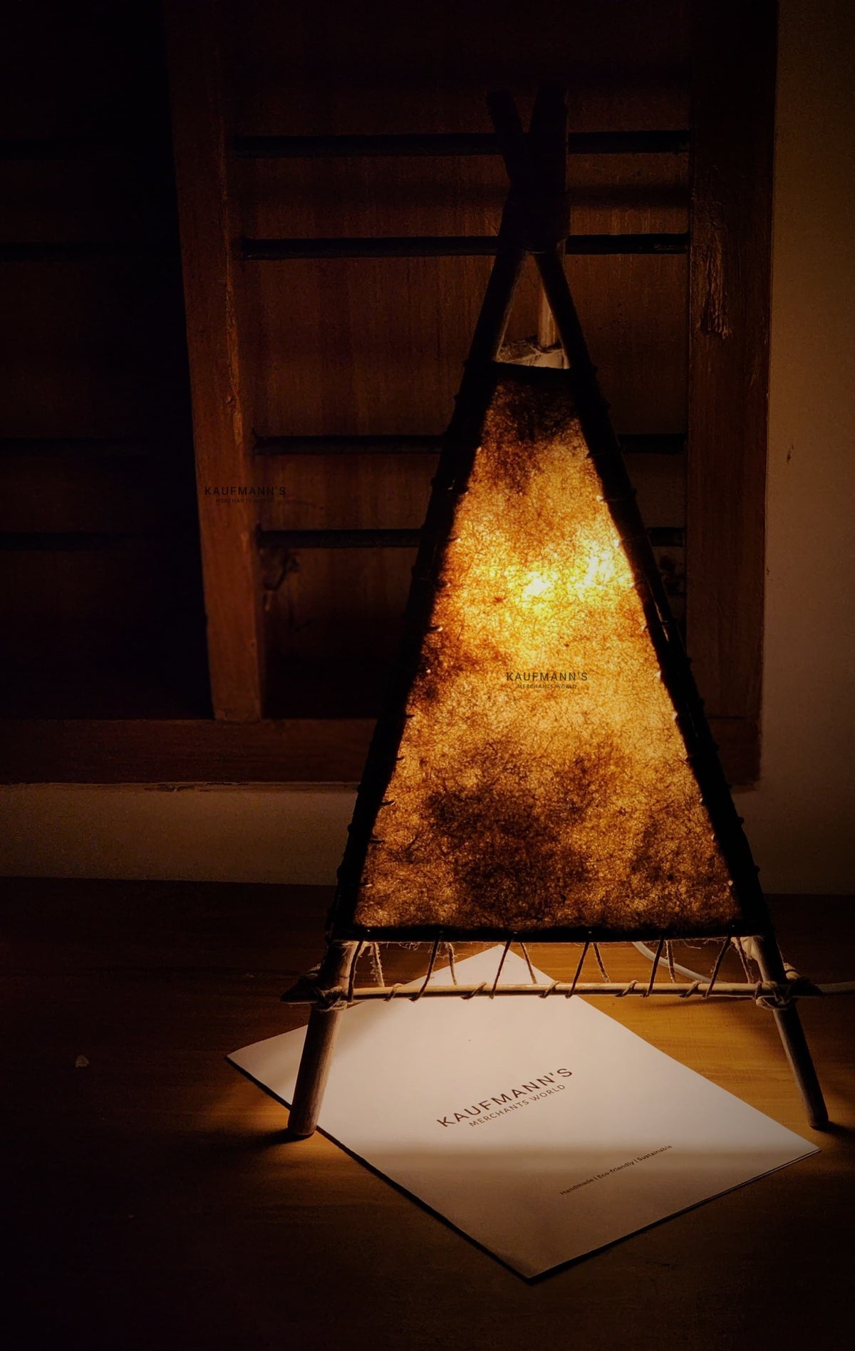 A handmade bamboo lampshade emitting a warm light, placed on a table with a piece of paper underneath.