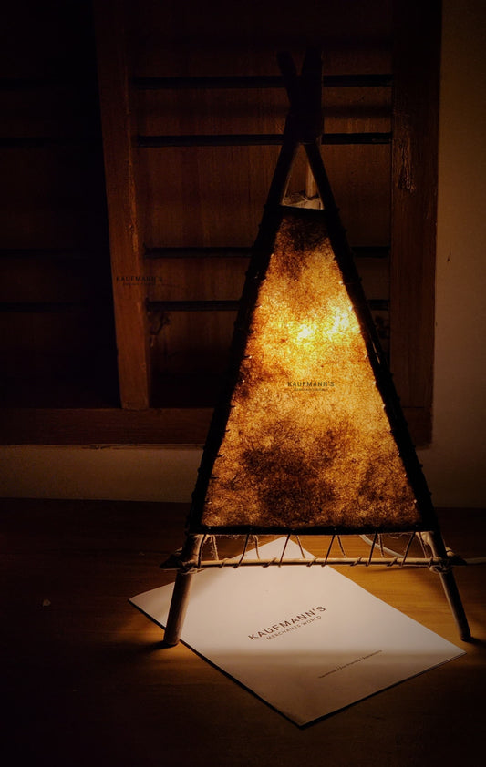 A handmade bamboo lampshade emitting a warm light, placed on a table with a piece of paper underneath.