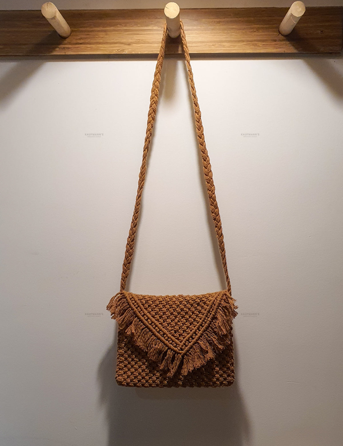 Brown woven handbag with tassels hanging on a wooden rack against a white wall.