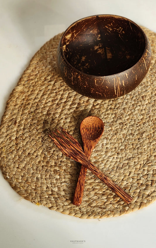 A beige coconut shell bowl with a cutlery set, including a spoon and a fork, on top of a textured beige surface.