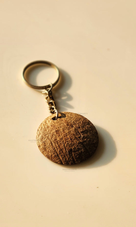 A handcrafted coconut shell key chain with a metal ring on a light background.