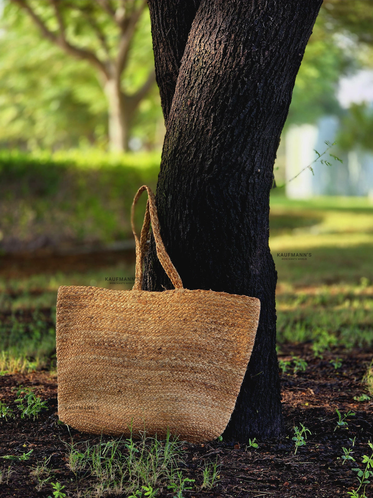 A beige coir tote bag hanging on a tree branch in a natural outdoor setting.