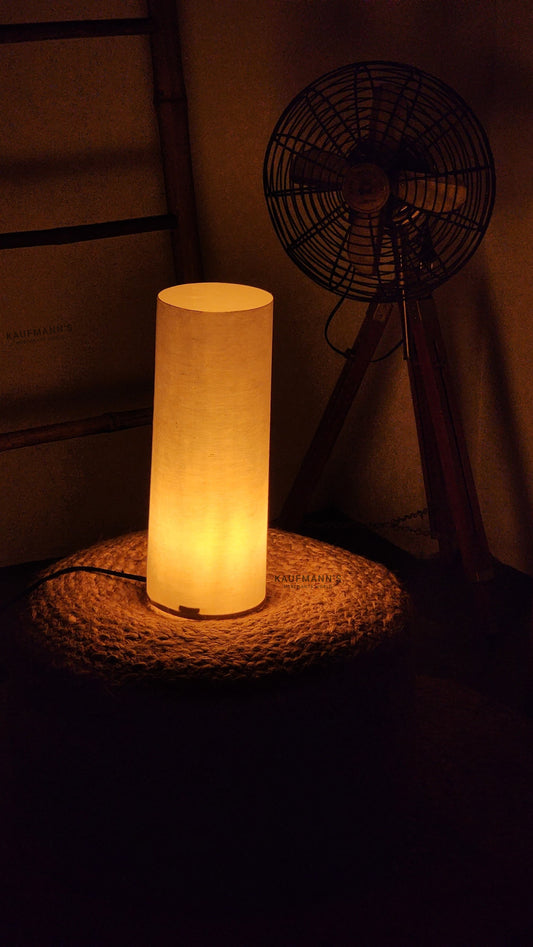 A handmade, eco-friendly paper  lampshade illuminated, placed on a rock surface with a fan and other light sources in the background.
