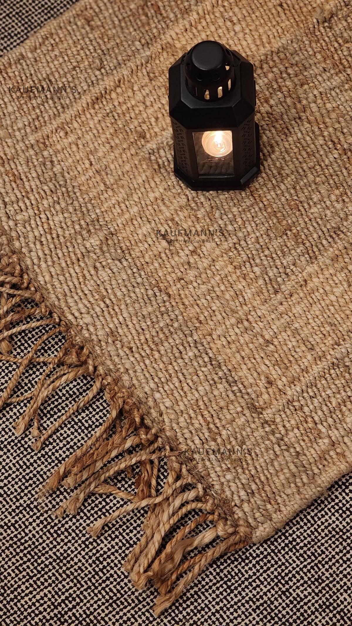 A beige jute rug with a fringed edge, placed on a textured background, showcasing its natural color and texture.