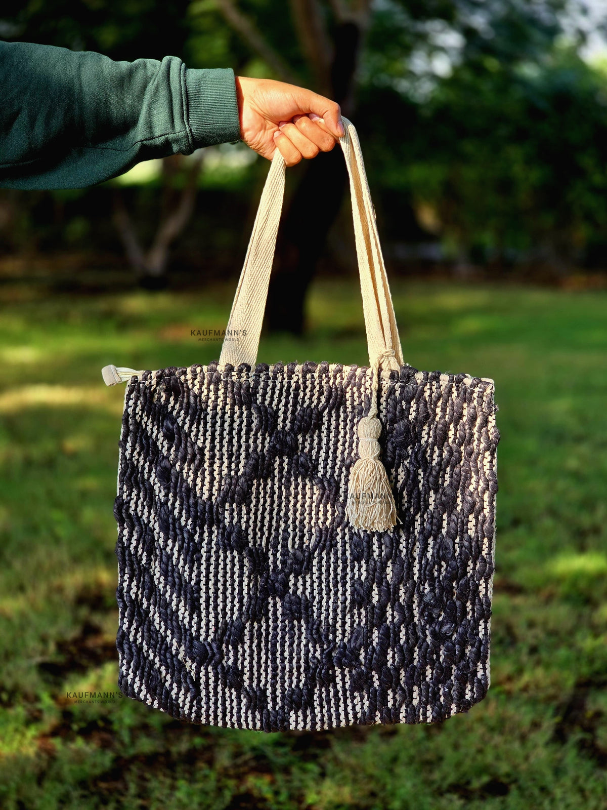A black and white Jute tote bag with handles, displayed in a natural outdoor setting.