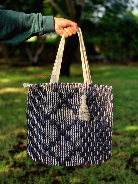 A black and white Jute tote bag with handles, displayed in a natural outdoor setting.