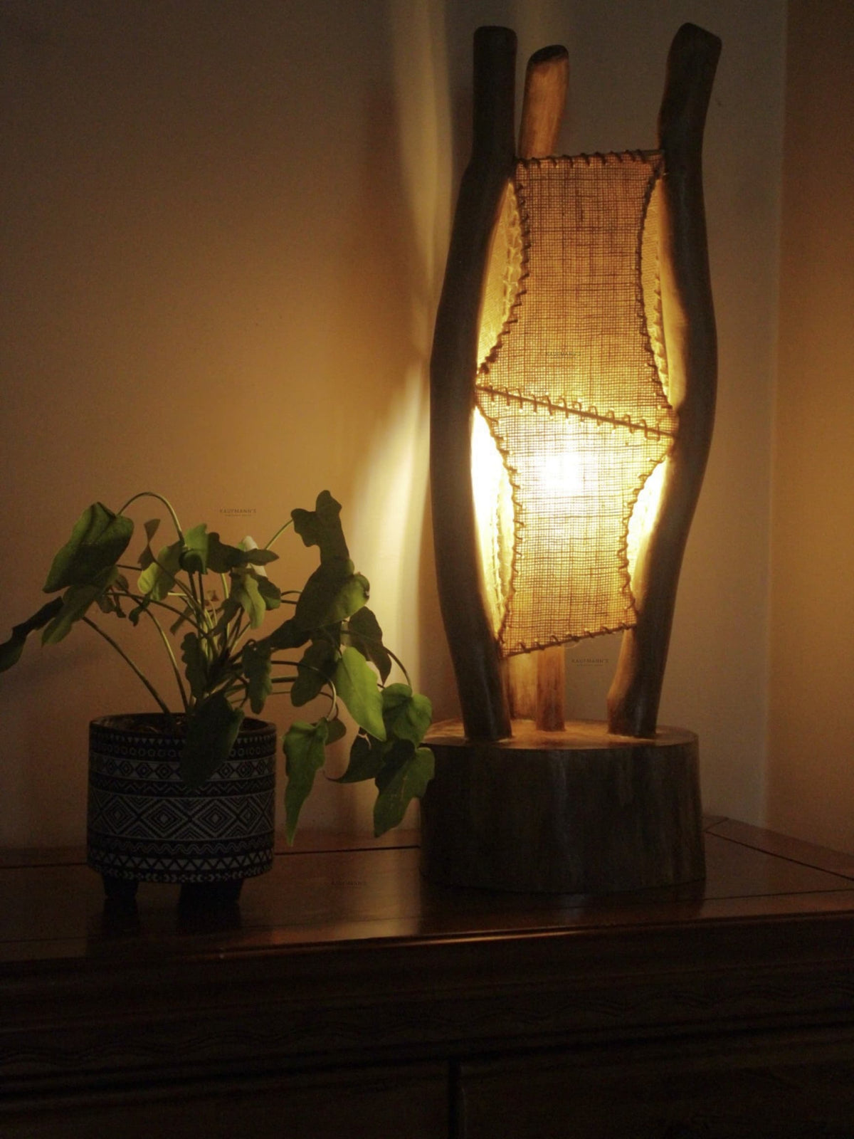 Wooden lamp with woven shade on a surface next to a plant