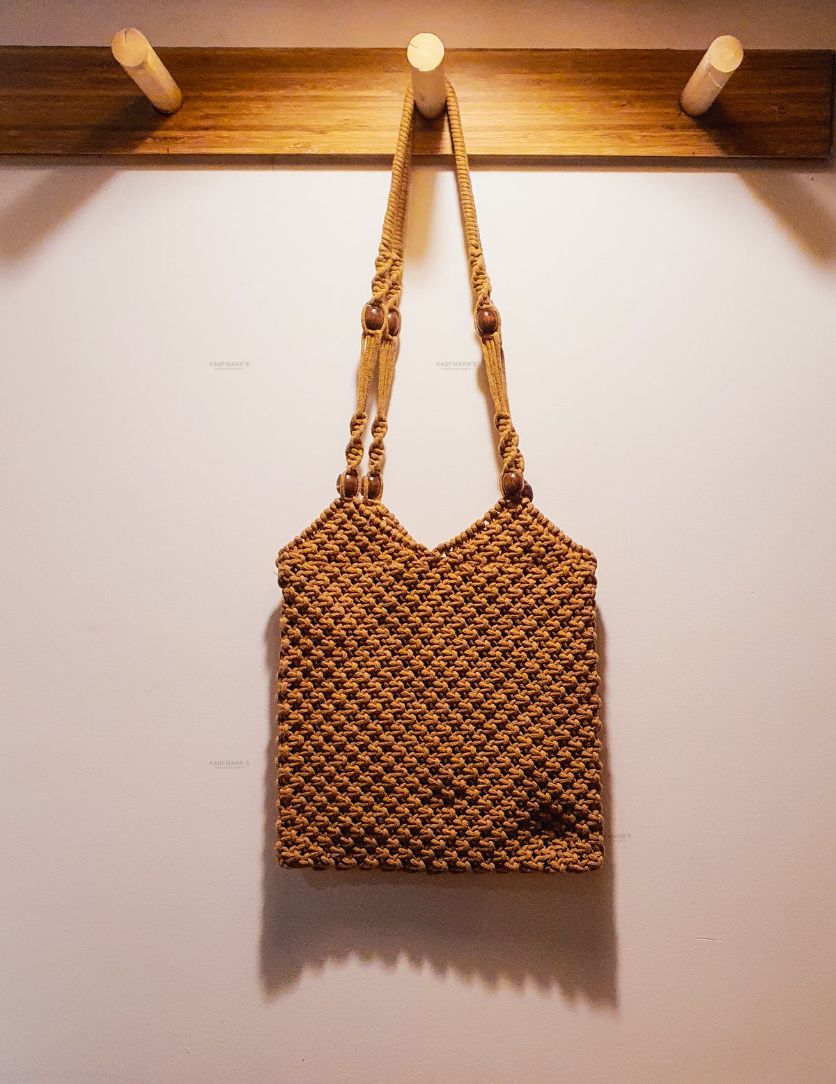 Brown woven handbag hanging on a wooden hook against a white wall