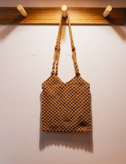 Brown woven handbag hanging on a wooden hook against a white wall
