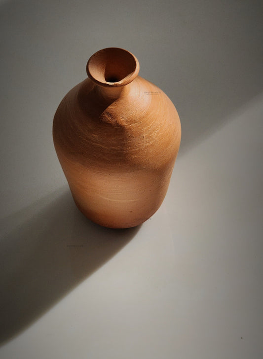 A handmade terracotta pot with a round shape and a visible natural earthy color, placed on a grey background.