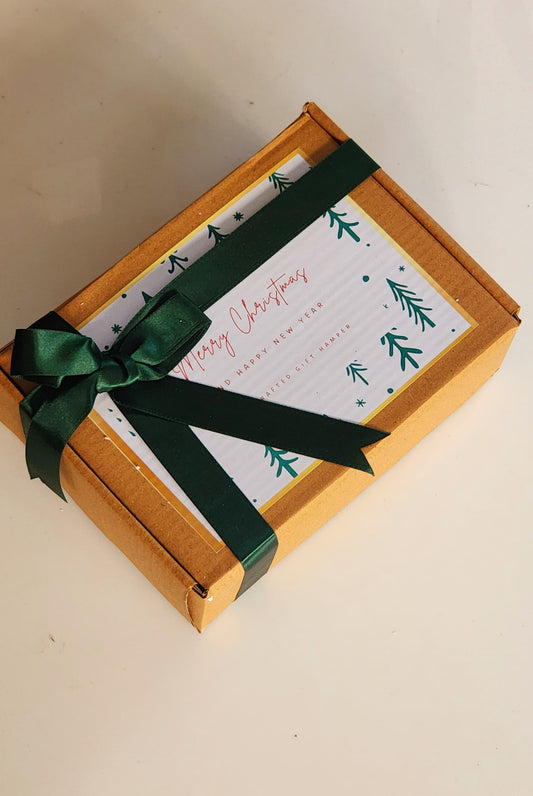 A gift hamper with a green ribbon, containing a card with 'Merry Christmas' and greenery designs, placed on a white surface.