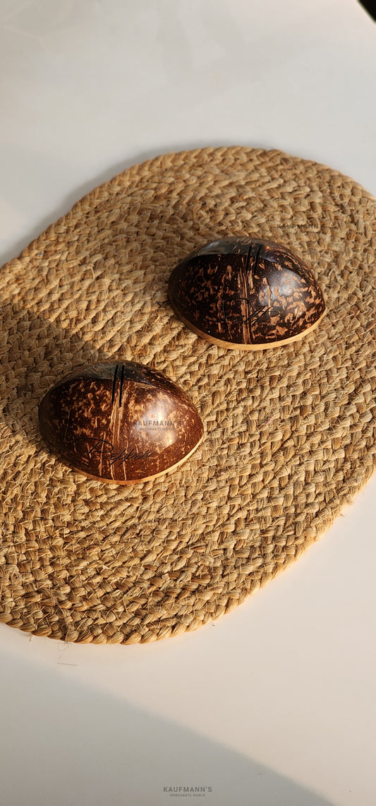 Two coconut shell salt or pepper shakers on a woven mat, with a textured background.
