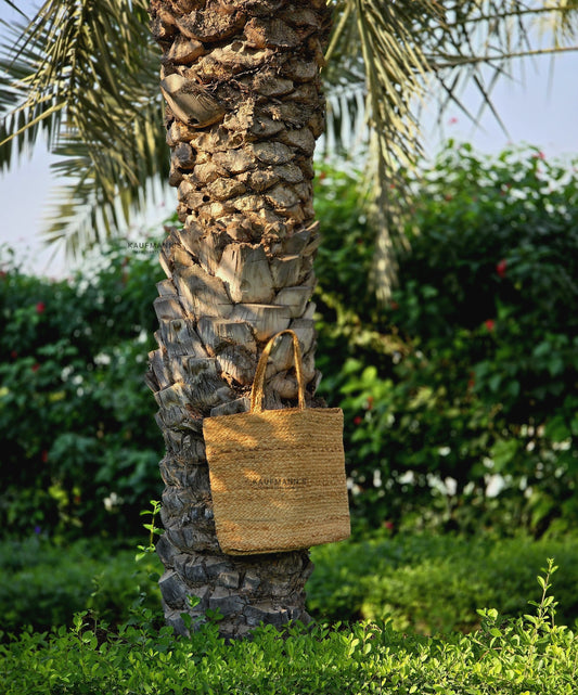 A handmade coir bag hanging on a tree, with a palm tree in the background.